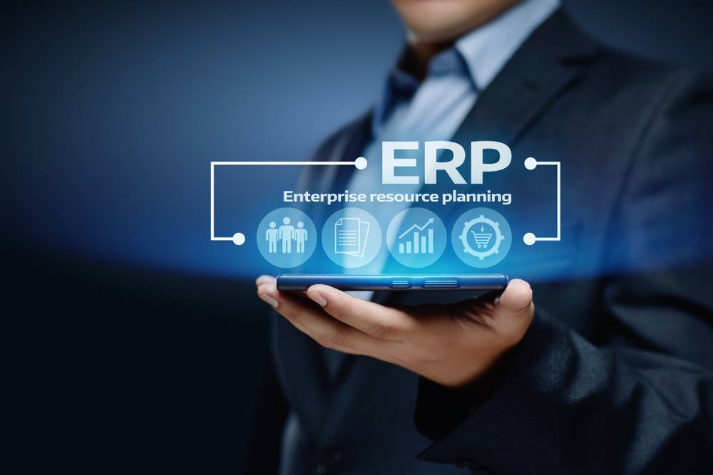 A businessman holds a tablet displaying a hologram reading “ERP.”