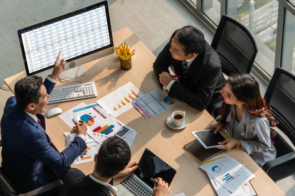 A business team gathered around a table, looking at spreadsheets.