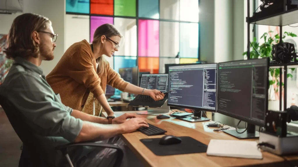 A man and woman looking at an array of computer monitors.