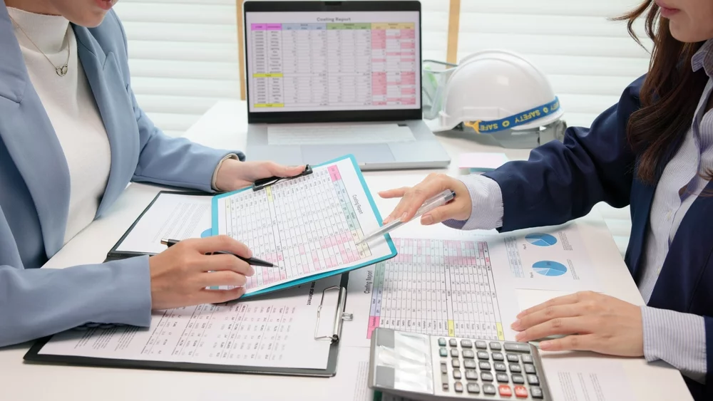 Two businesswomen looking a spreadsheets and a laptop.