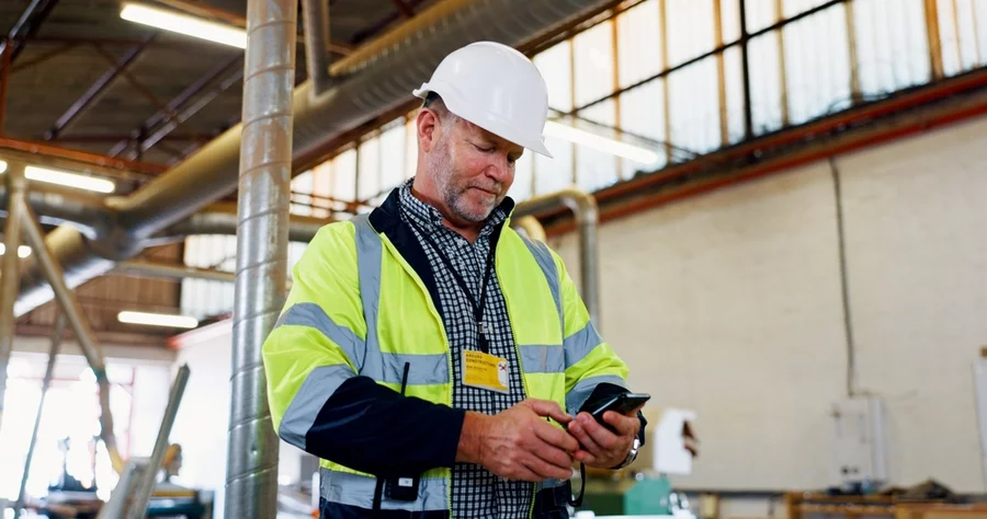 A man in a warehouse wearing PPE and using a phone.