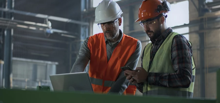 Two technicians in an industrial facility, looking at a laptop and wearing PPE.